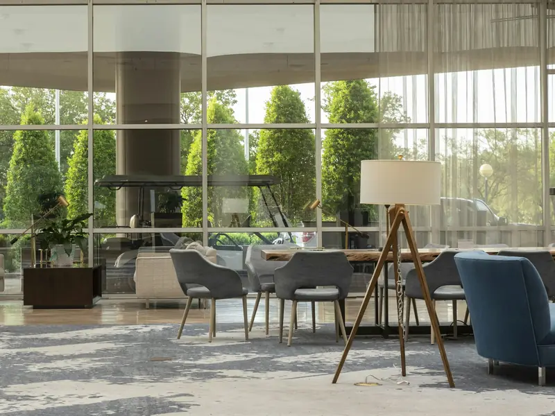 Hotel lobby lounge with upholstered chairs and a long table in front of floor-to-ceiling windows